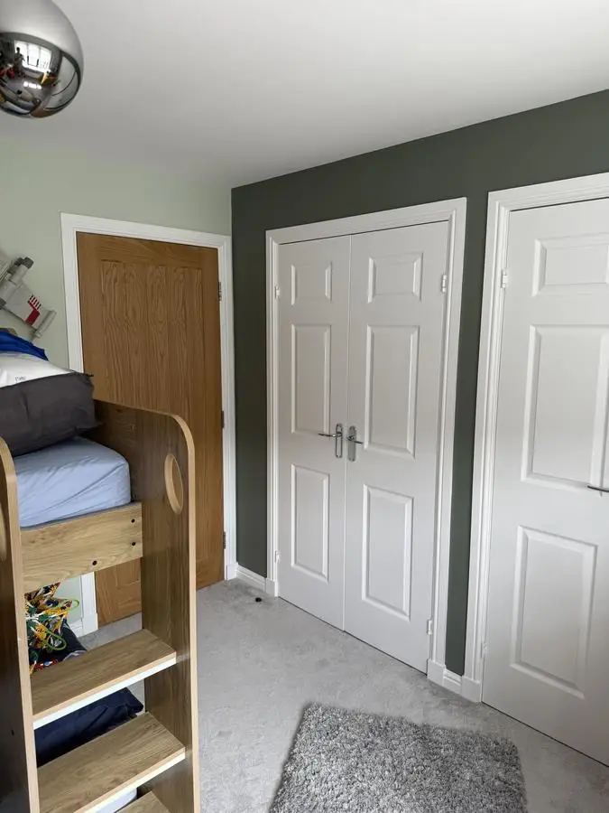 Bedroom with a deep green feature wall and white panelled wardrobe doors