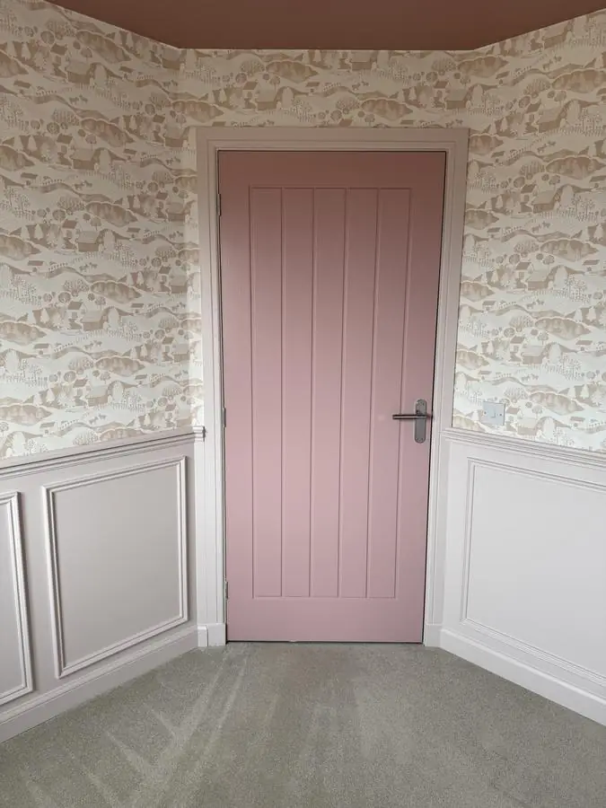 Child's bedroom with patterned wallpaper above pink painted wall panelling and a pink door