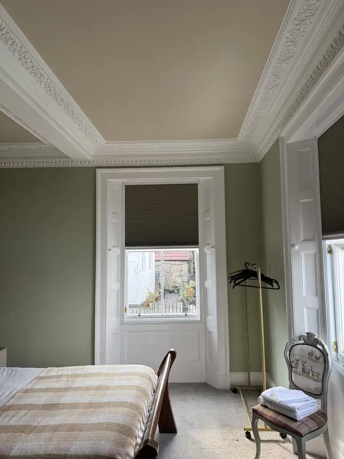 Hotel bedroom decorated in soft sage green with white cornicing
