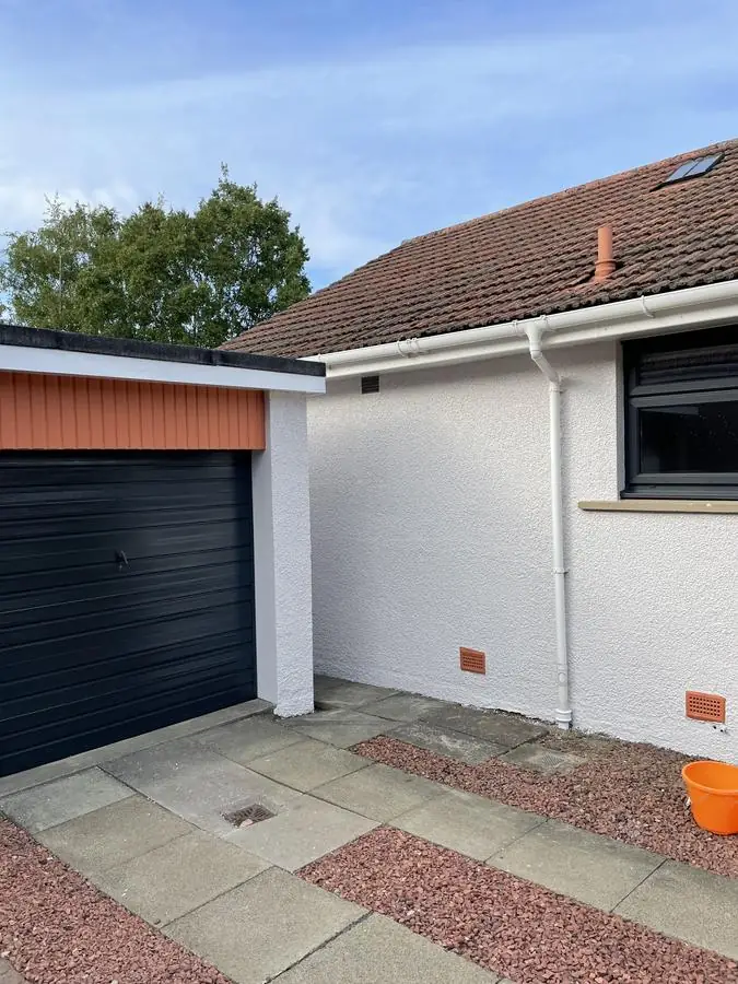 White painted render and a dark garage door on a detached house