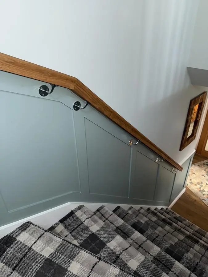 Staircase wall panelling painted soft green beneath a timber handrail