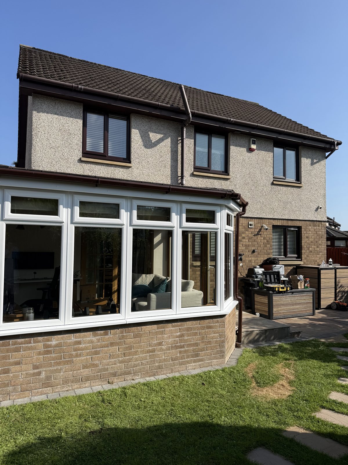 Rear of a house with dark brown UPVC window frames, fascias and gutters above a white UPVC conservatory